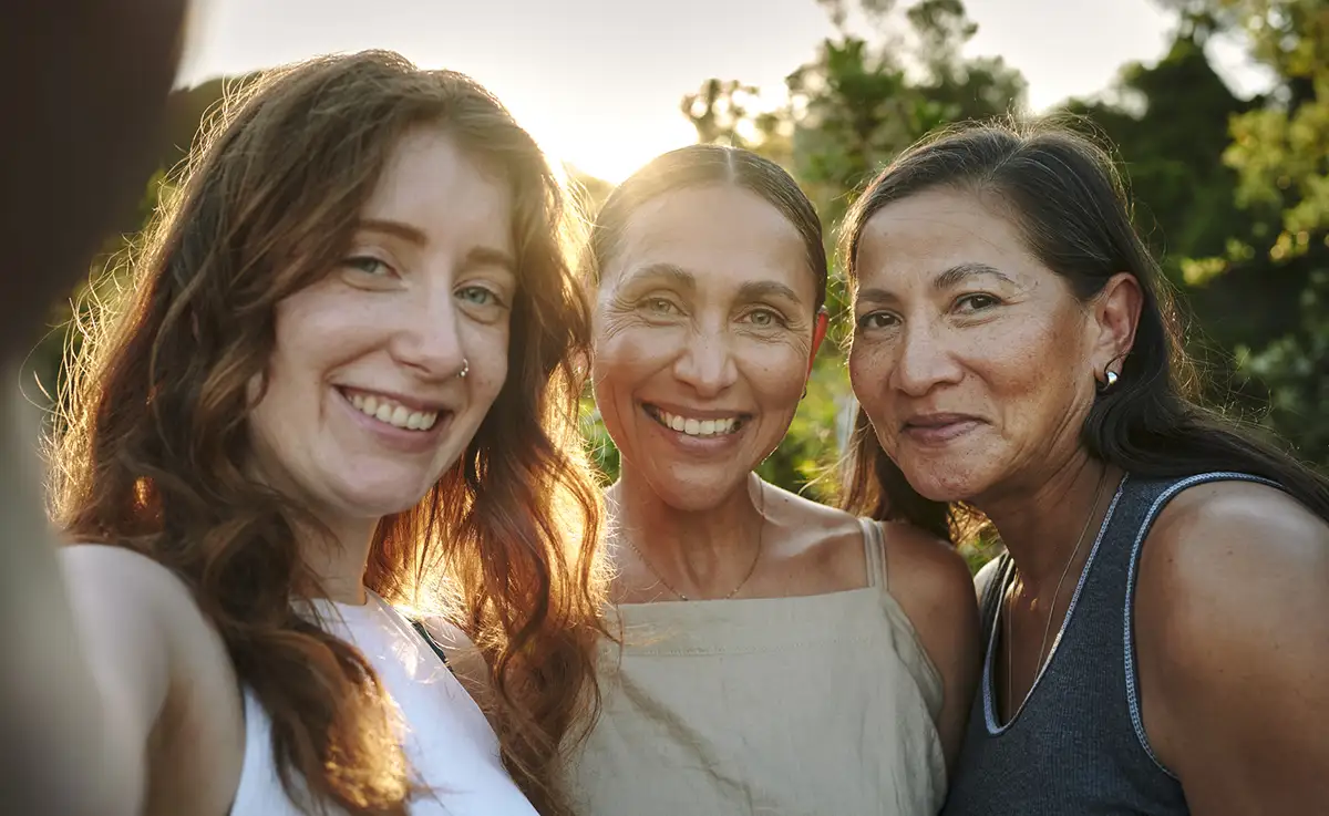 Three women taking a selfie with the sun setting behind them