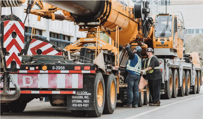 workers are standing in front of a large truck with a crane