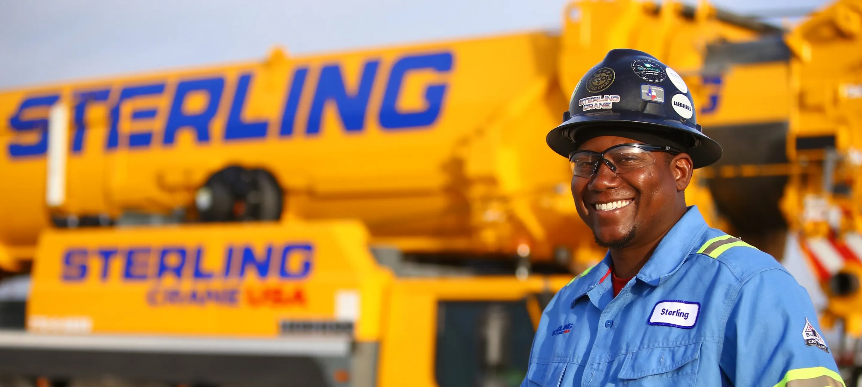 there is a man in a hard hat and overalls standing in front of a crane