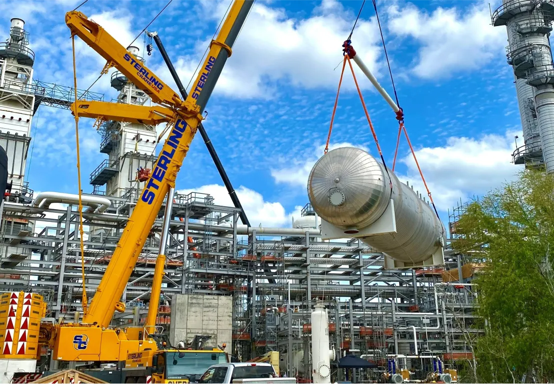 crane lifting a large tank onto a construction site
