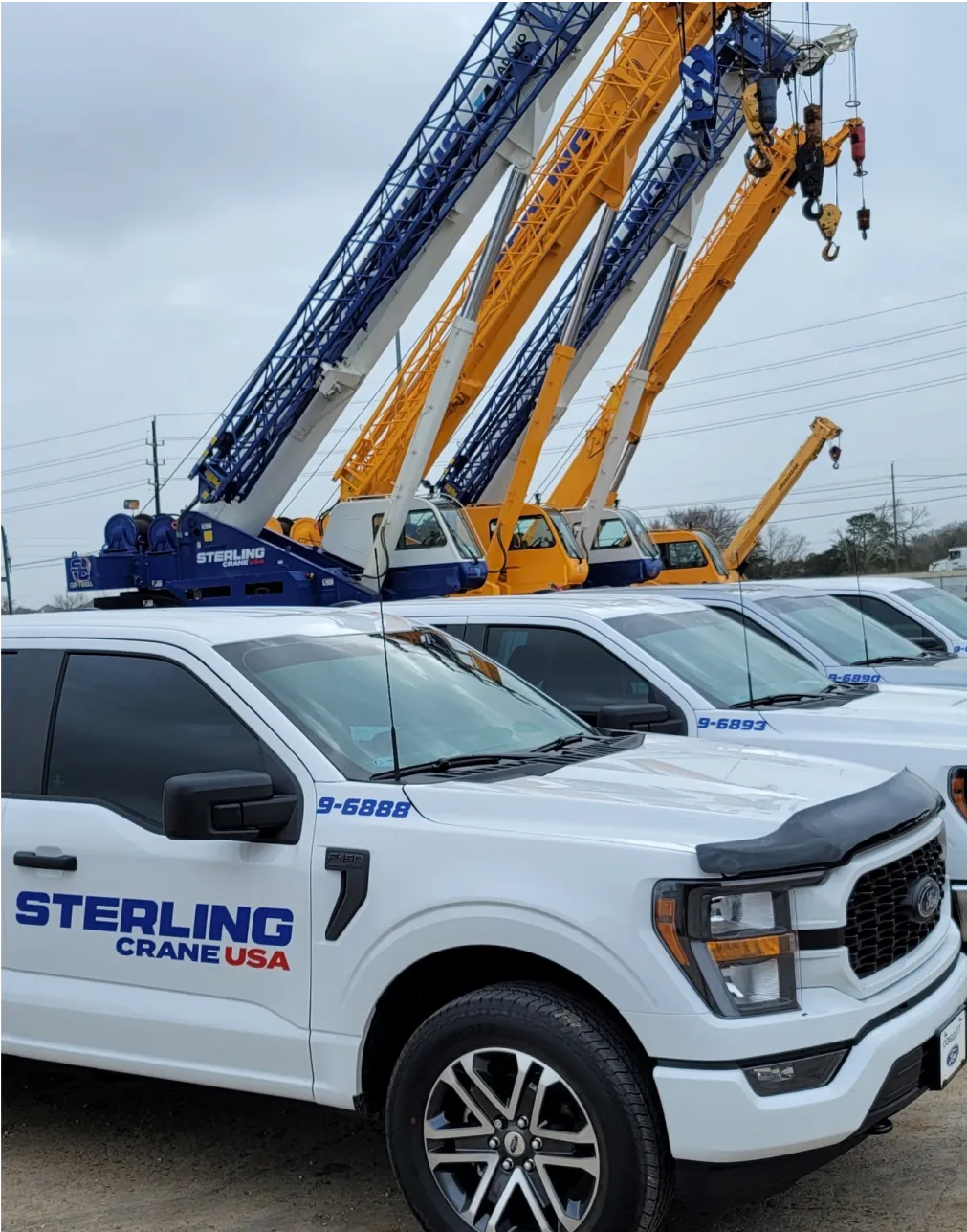 several white trucks are parked in a lot with a crane on top