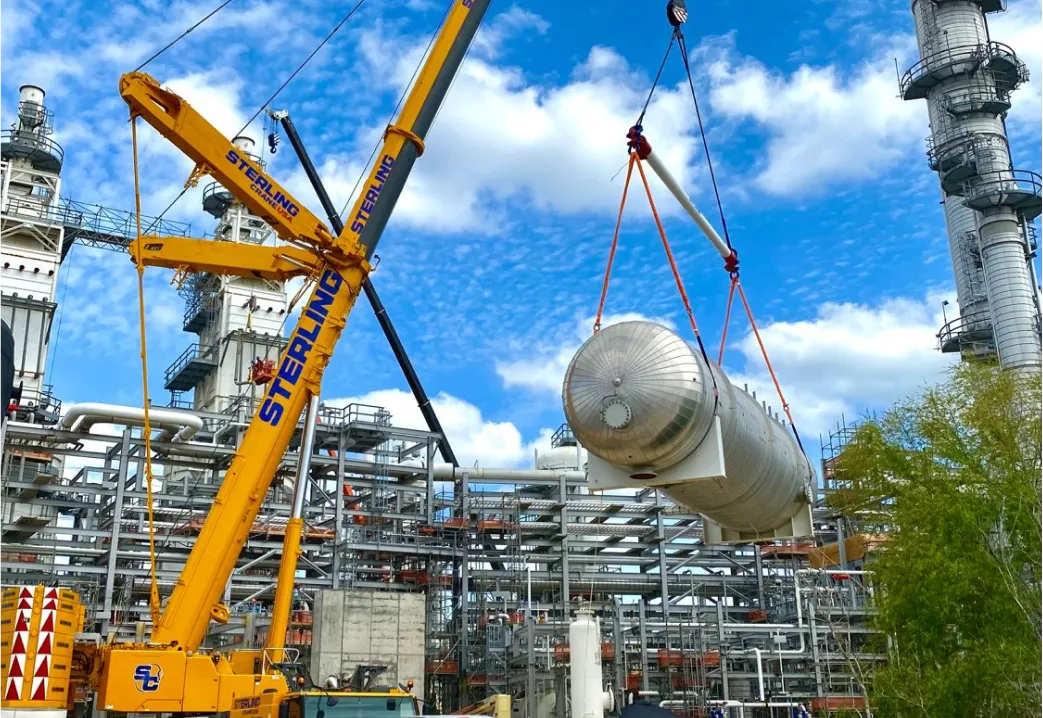 crane lifting a large metal object in front of a large building