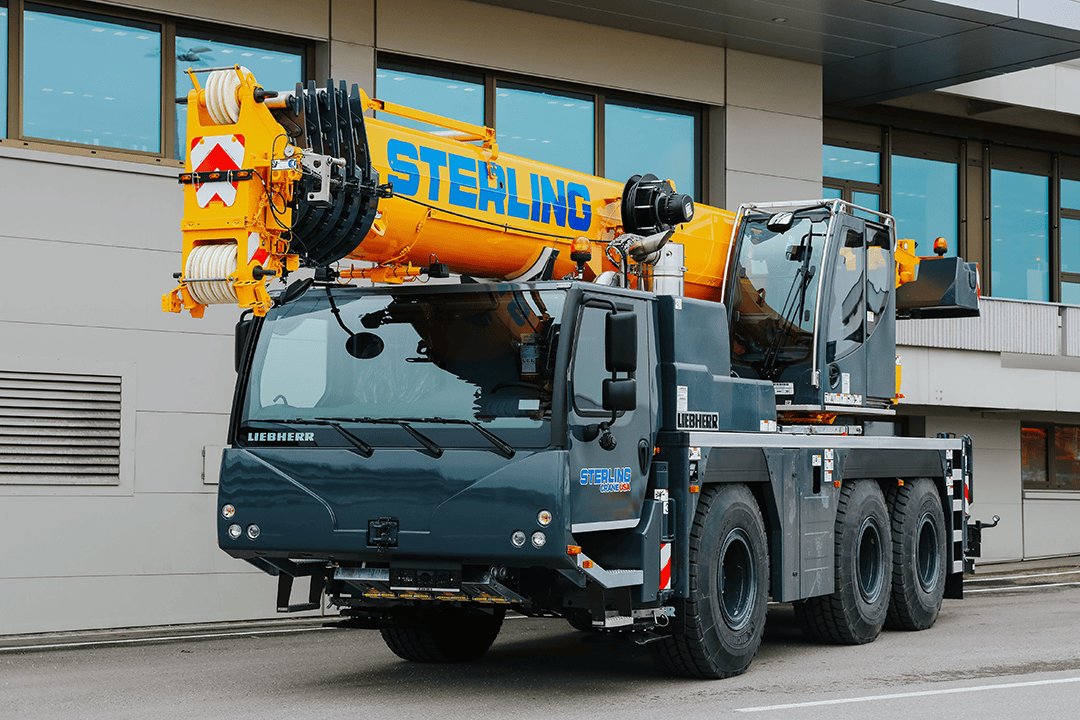 A large yellow truck with a man on a motorcycle. Sterling Crane - Leaders in Crane Rentals & Services.