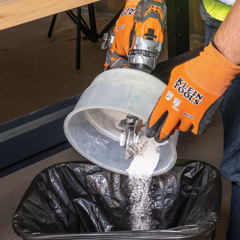 Worker emptying dust and debris from Klein Tools collapsible dust bowl into a bin after drilling. Click to shop the Klein Tools Dust Bowl.
