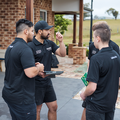 A team of electricians having a discussion while referencing a tablet and holding product boxes — click to join Club Clipsal.
