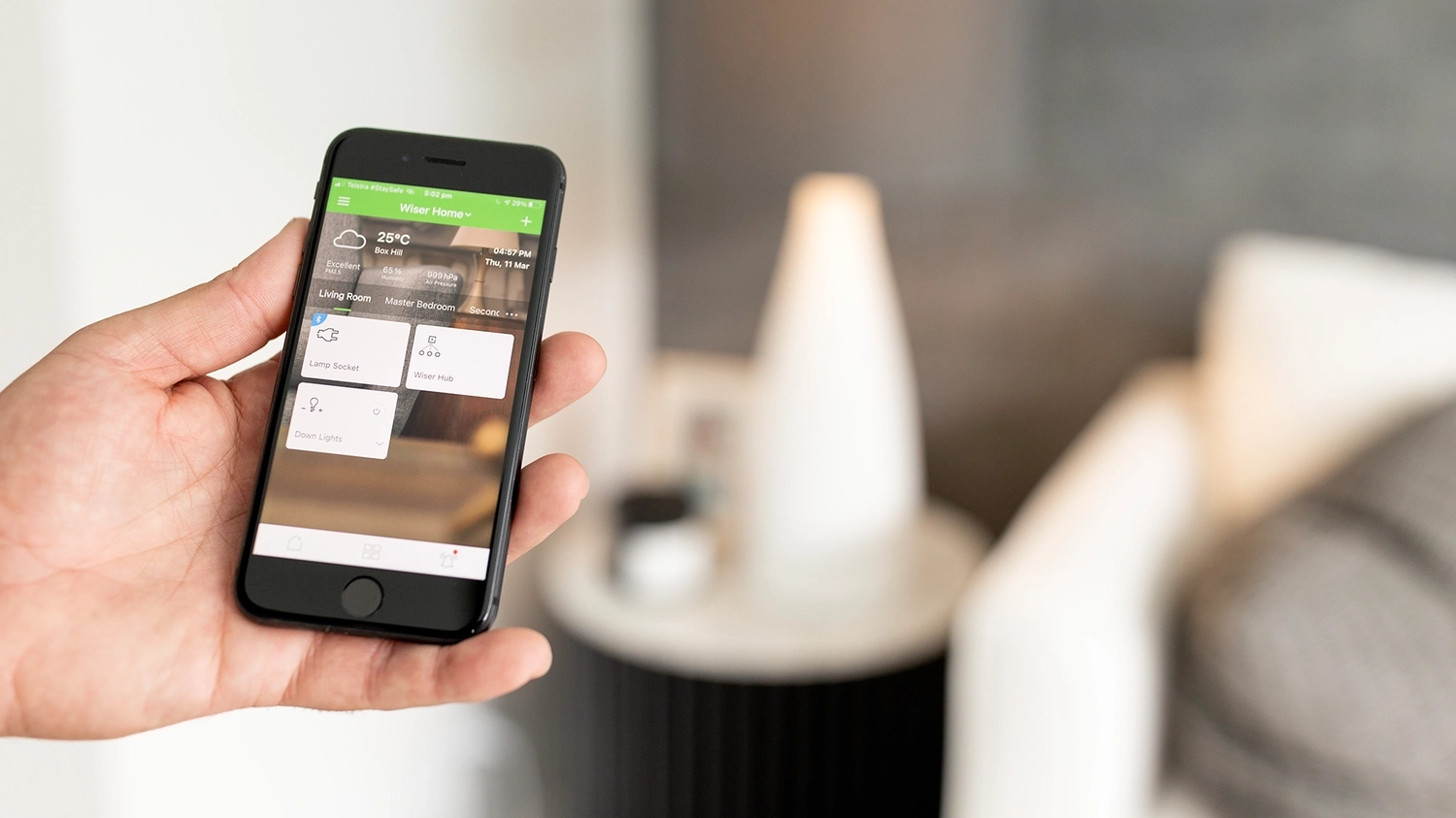 A hand holding a smartphone with the Clipsal Wiser™ app open to home automation controls - click here to shop Wiser now.