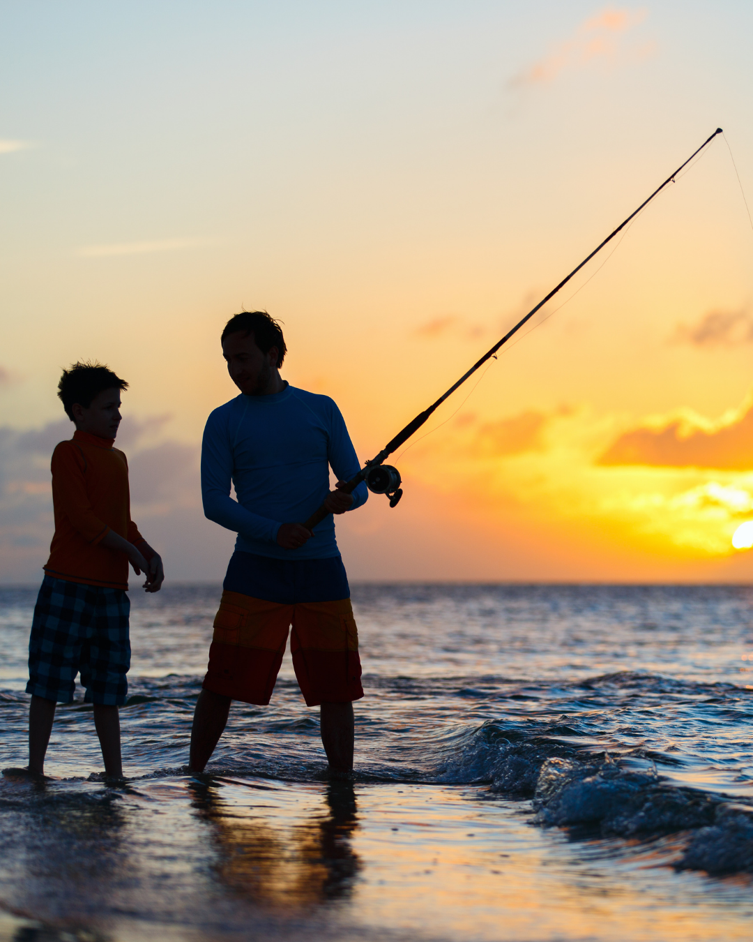 Silhouette of father and child fishing in shallow surf at sunset