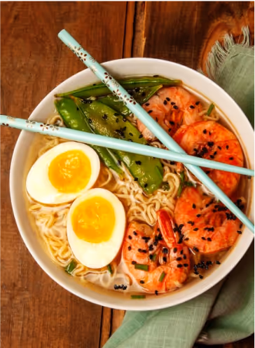 A bowl of spicy shrimp ramen with chop sticks laying on top. 