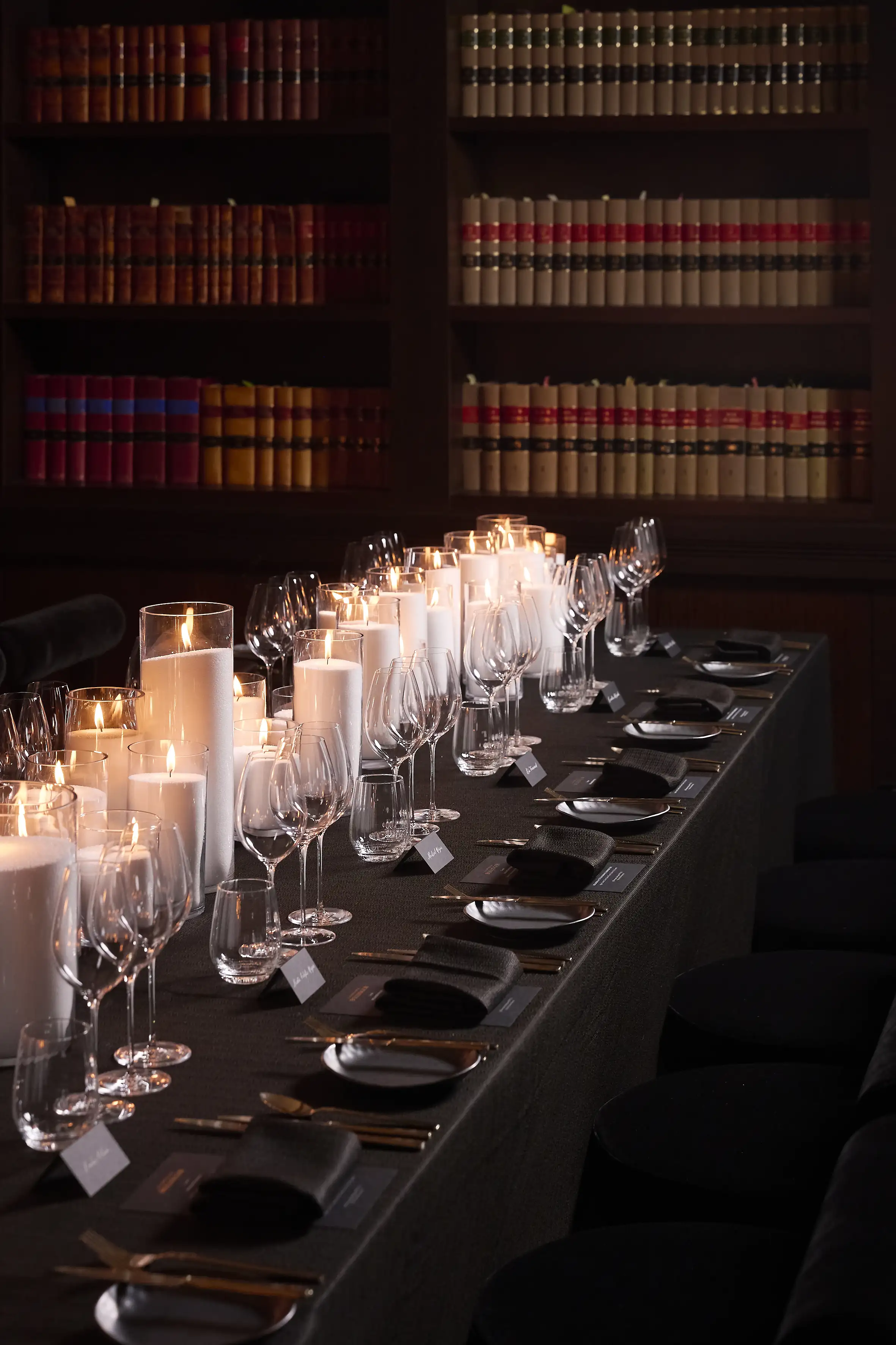 Long table set for an intimate candlelit dinner in a library.