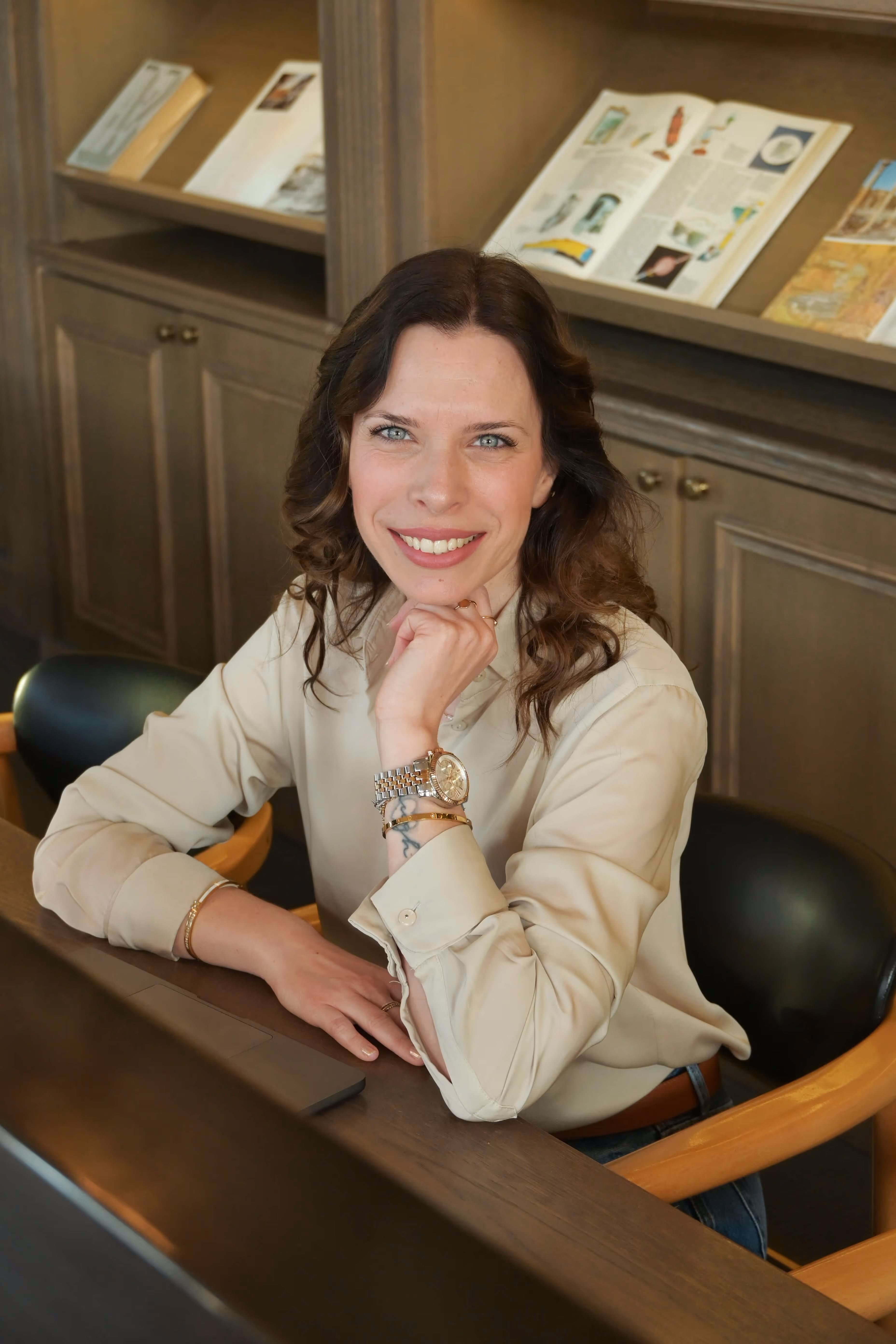 Matea Macan u svijetloj košulji sjedi za stolom i nasmiješena gleda u kameru.