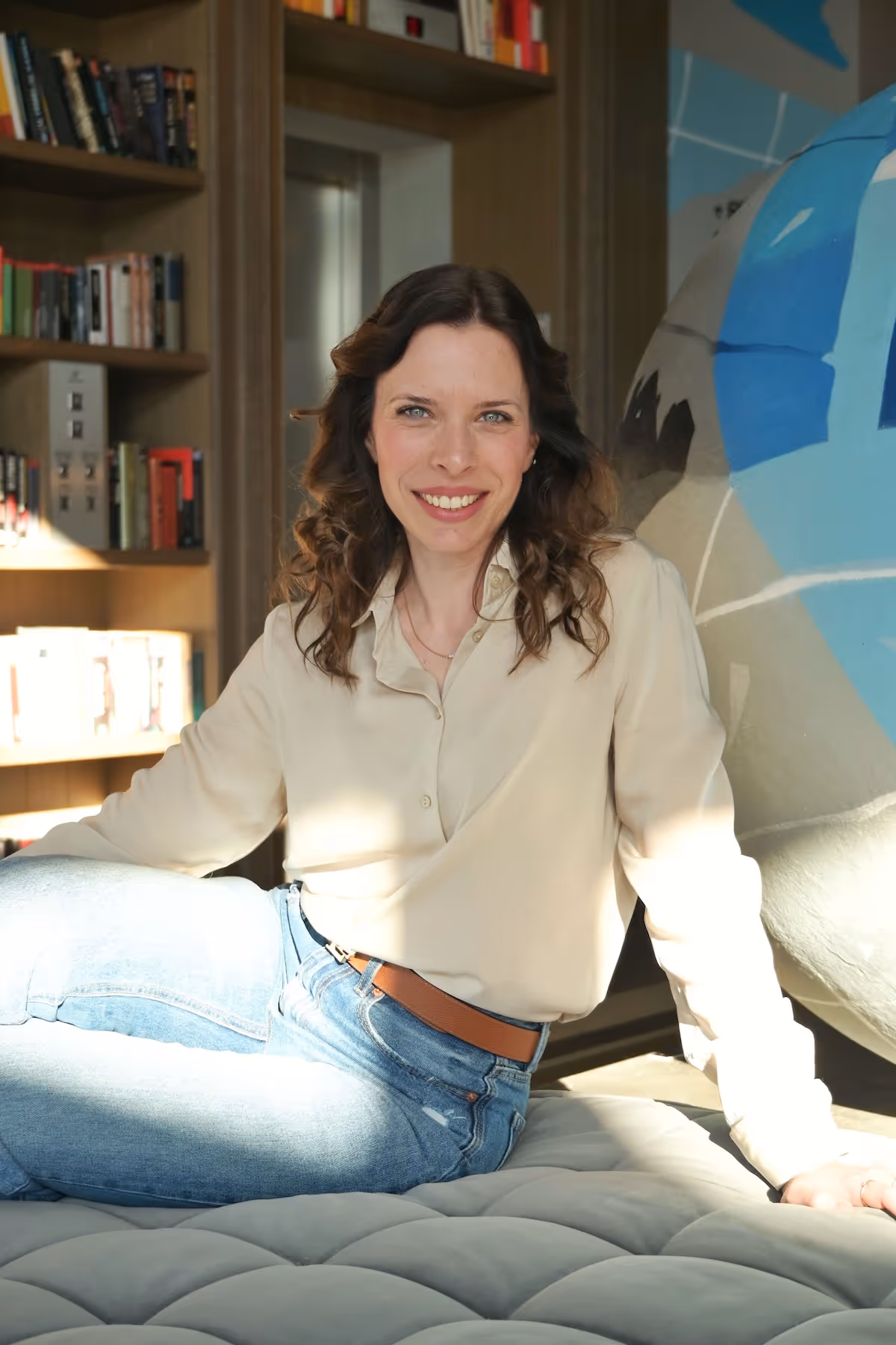 Matea Macan sjedi naslonjena na sivu površinu, s policom knjiga u pozadini.