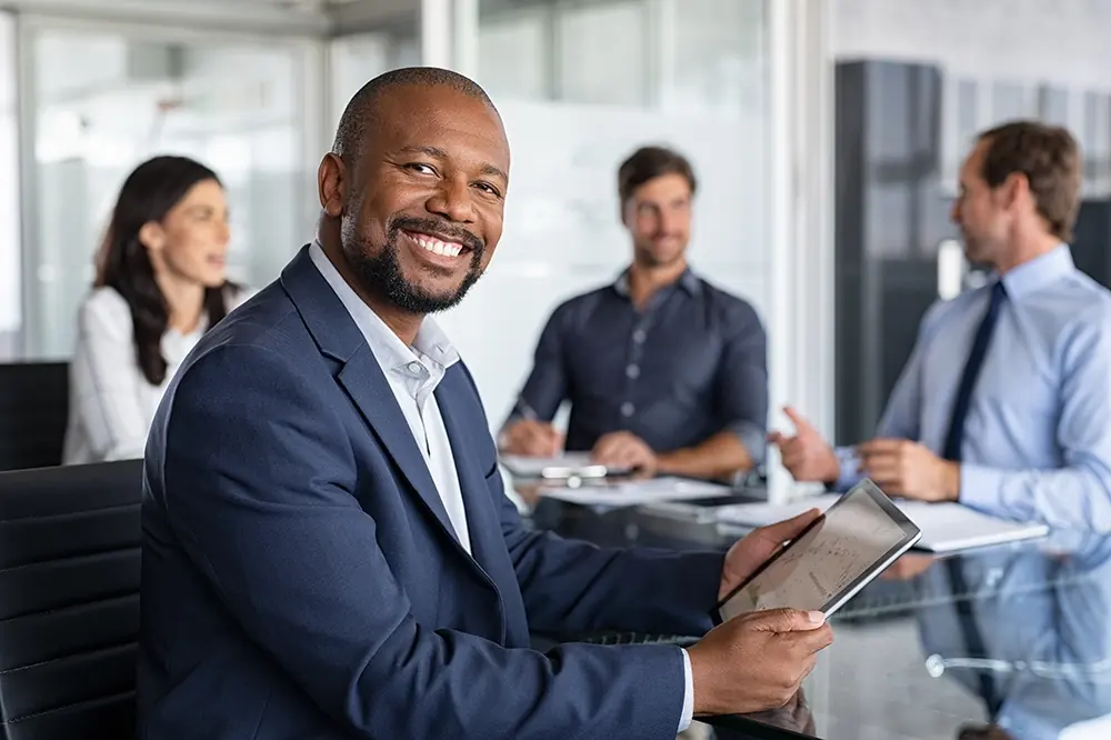 A smiling finance professional in a business suit holding a digital tablet in a modern boardroom, representing capital providers using GPS-verified data and AI-validated invoices to fund utility contractor receivables with confidence.