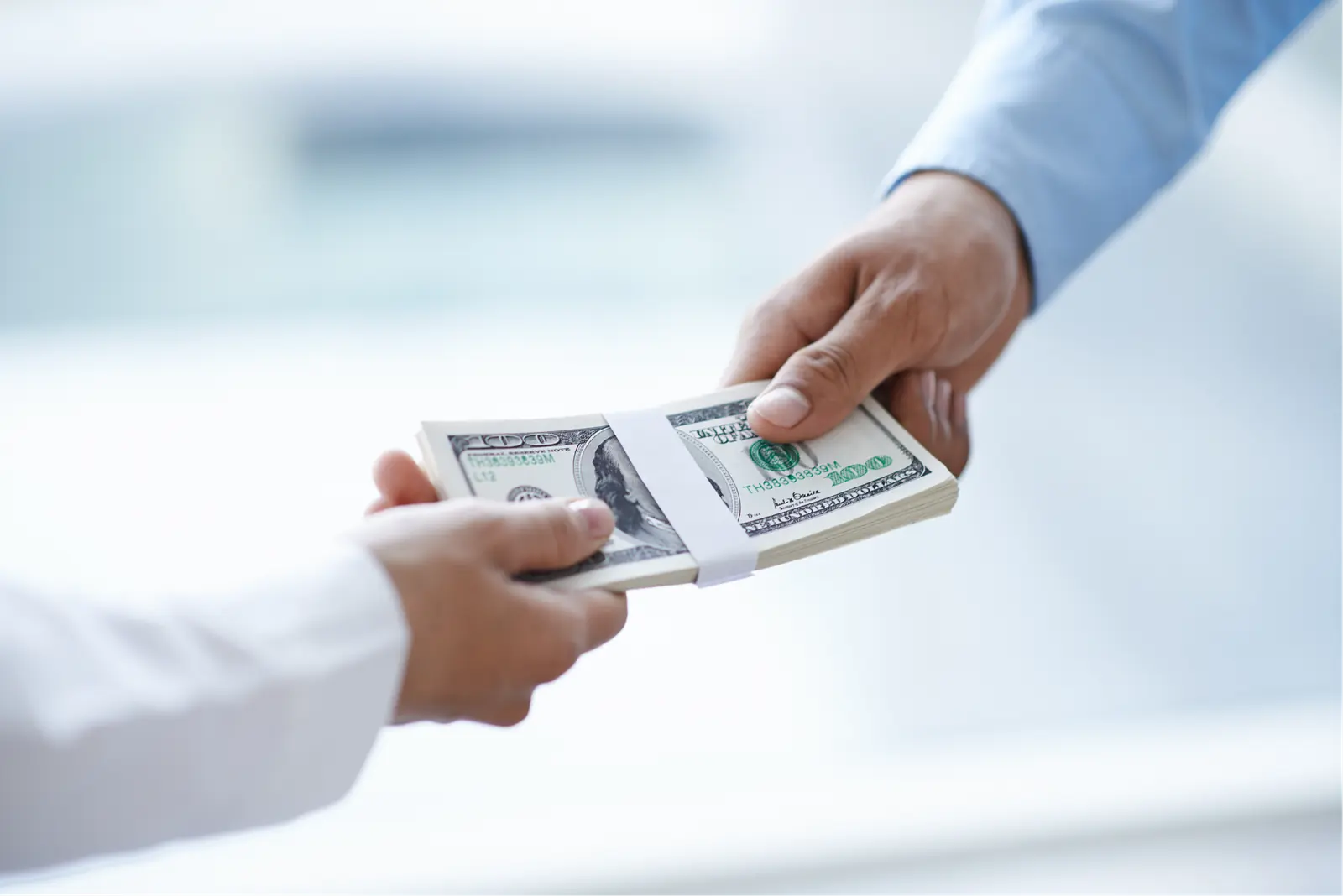 Two people exchanging a stack of US dollar bills.