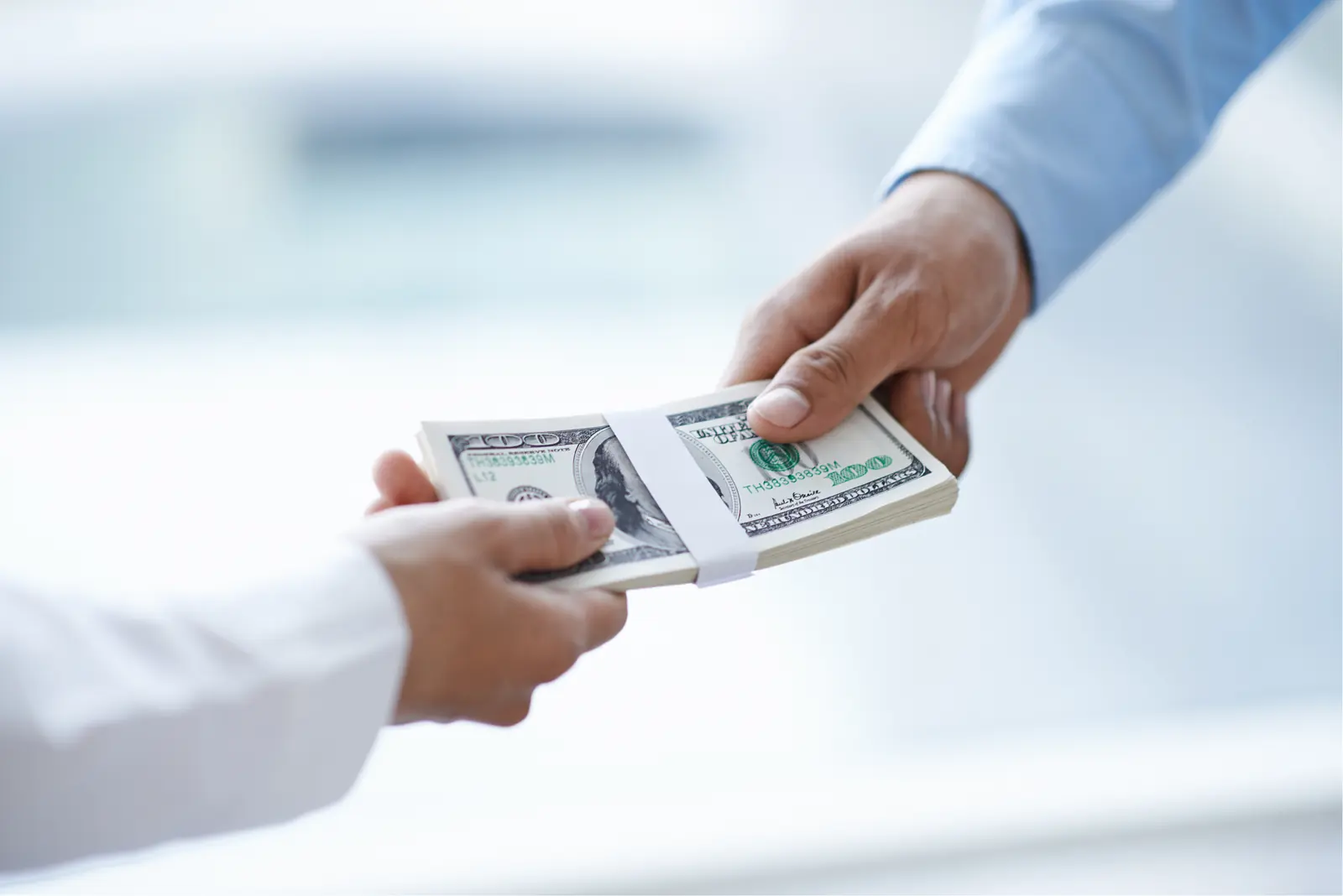 Two people exchanging a stack of US dollar bills.