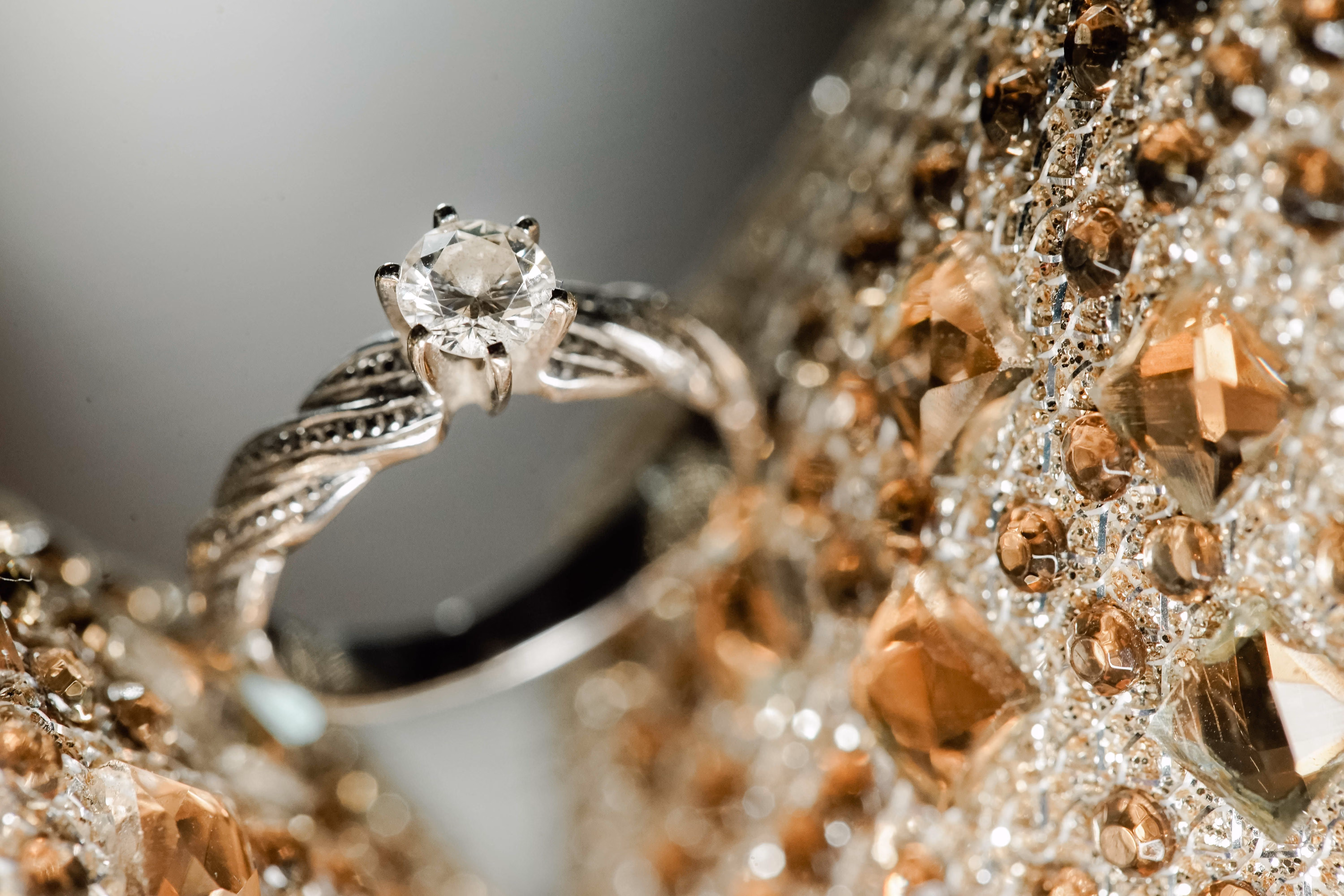 Bague en argent avec un diamant taillé rond fixé par six griffes, posée sur un fond de nombreuses petites pierres dorées facettées.