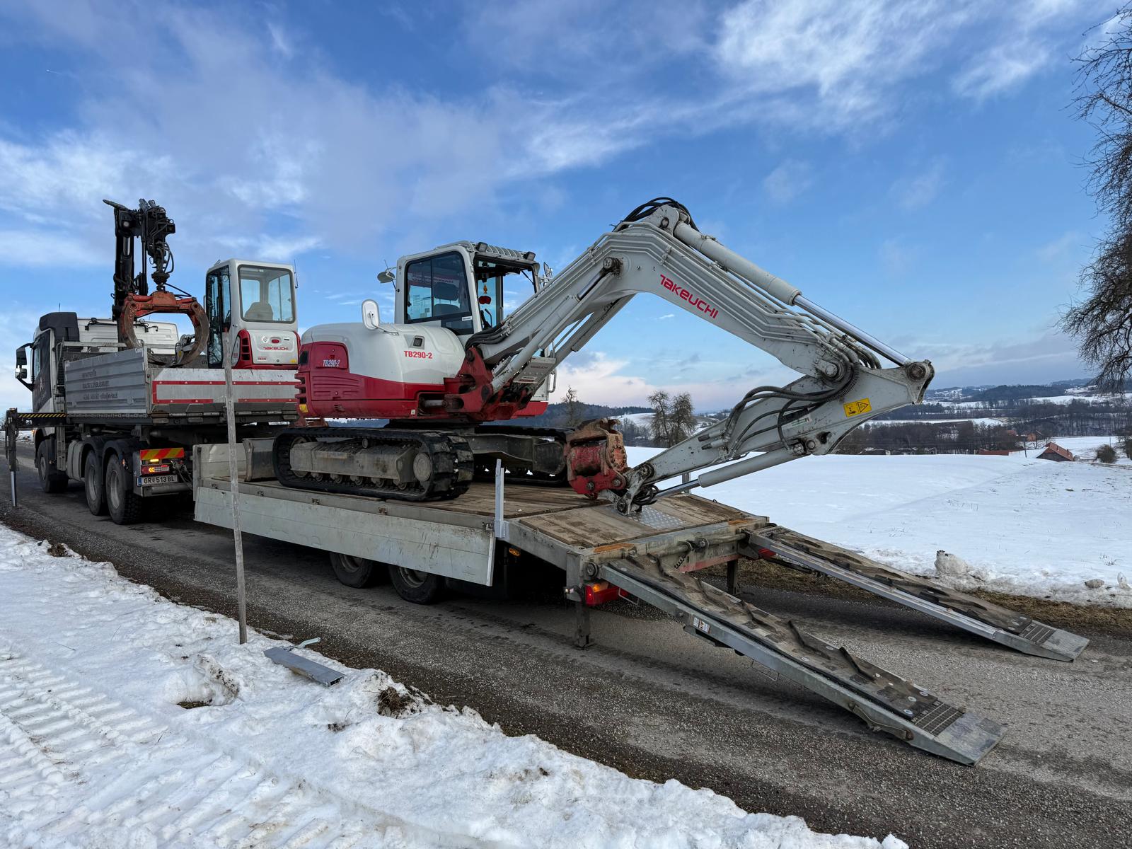 Ein Lastwagen mit Anhänger transportiert zwei Takeuchi-Bagger an einem winterlichen Landstraßenrand.