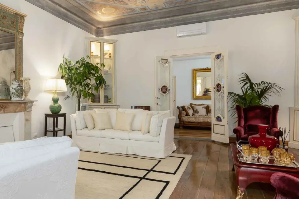  An elegantly furnished living room with a white sofa, red armchair, a patterned rug, and ornate ceilings.