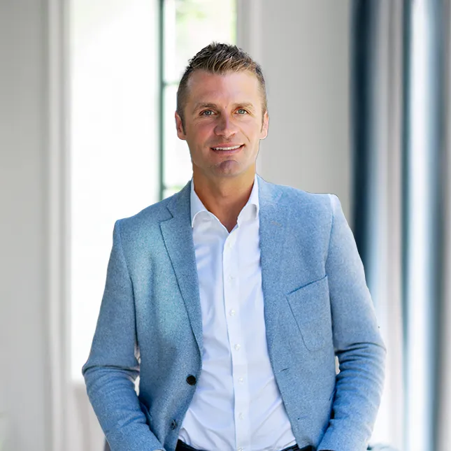 Color headshot of a man with short, light brown hair, smiling in a light blue blazer and white shirt.