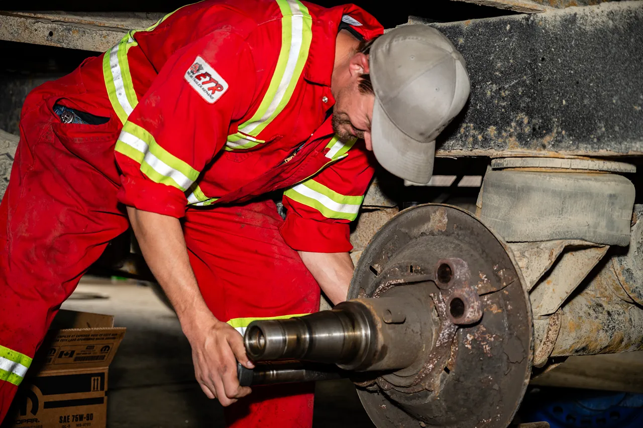 Technician performing trailer axle repair by removing the wheel hub. Coveralls display the text “CTR.”