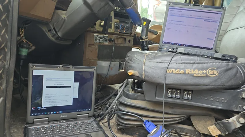 Two diagnostic laptops connected inside a heavy-duty truck cab for electronic troubleshooting, with a Wide Ride+ seat.