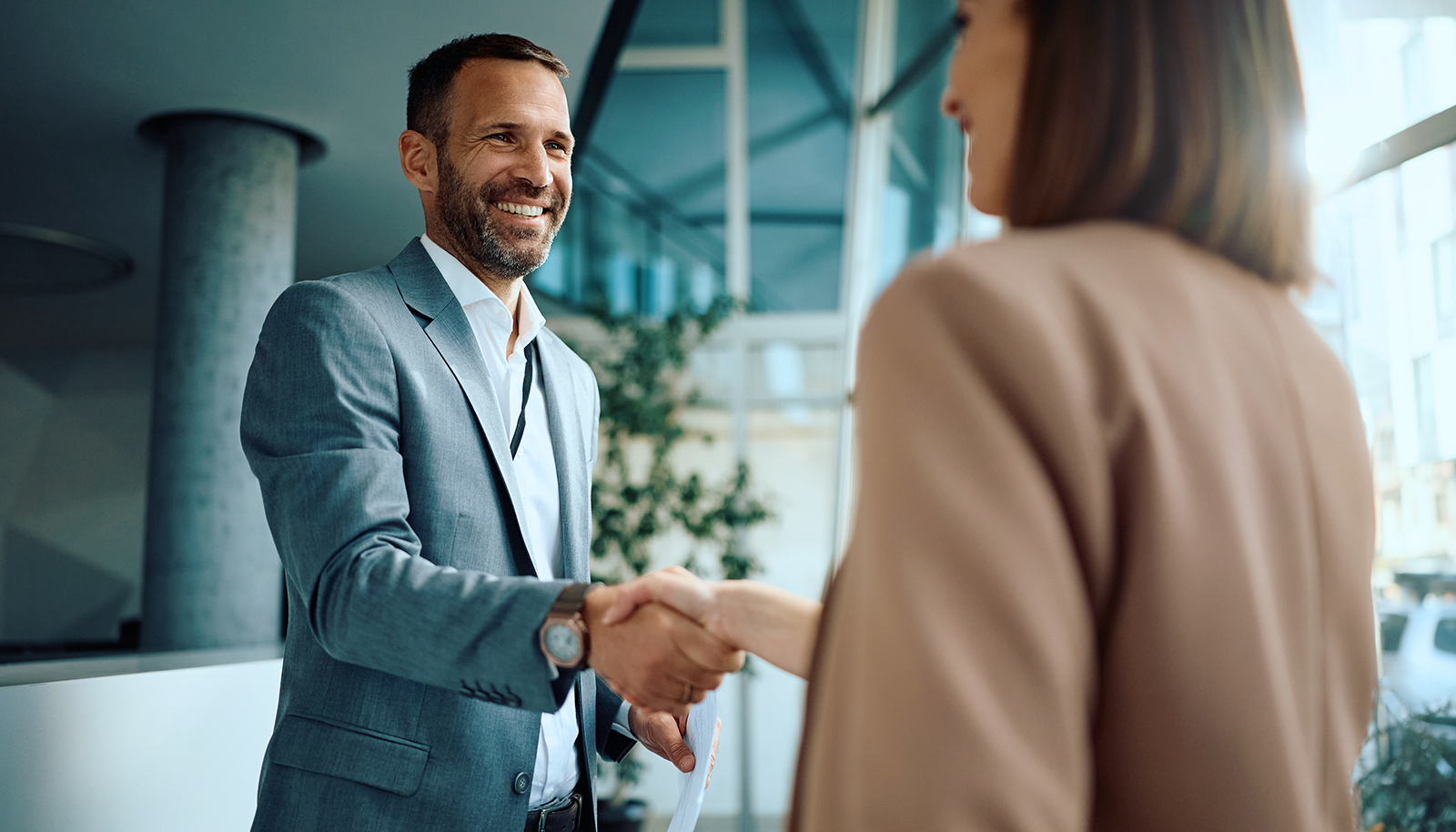 homem de terno apertandoa a mão de uma mulher de cabelos castanhos. Ambos sorridentes e fechando negócio.