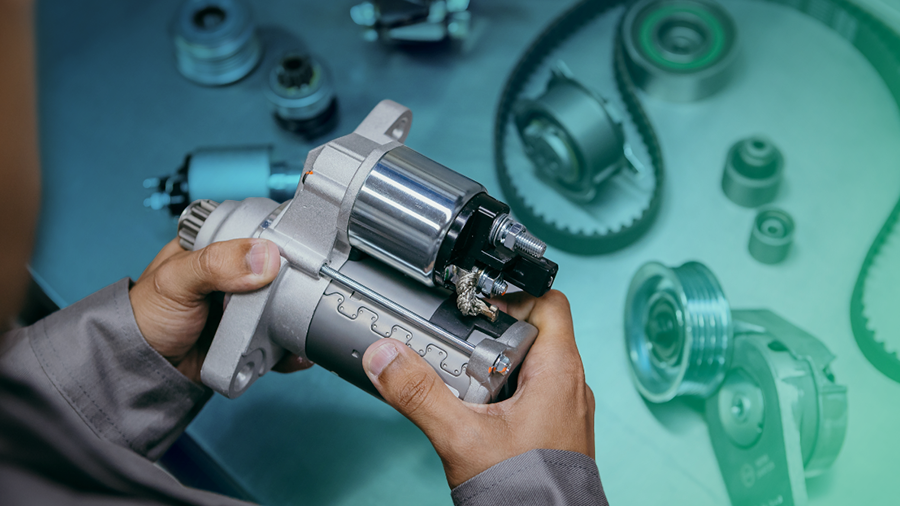 Técnico da indústria automotiva segurando impulsor de partida desmontado, ao lado de outras peças automotivas 