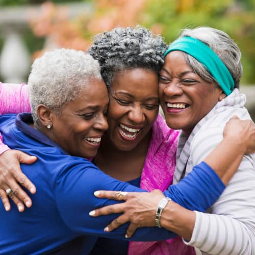 A group of older black women embracing each other with smiles on their faces.