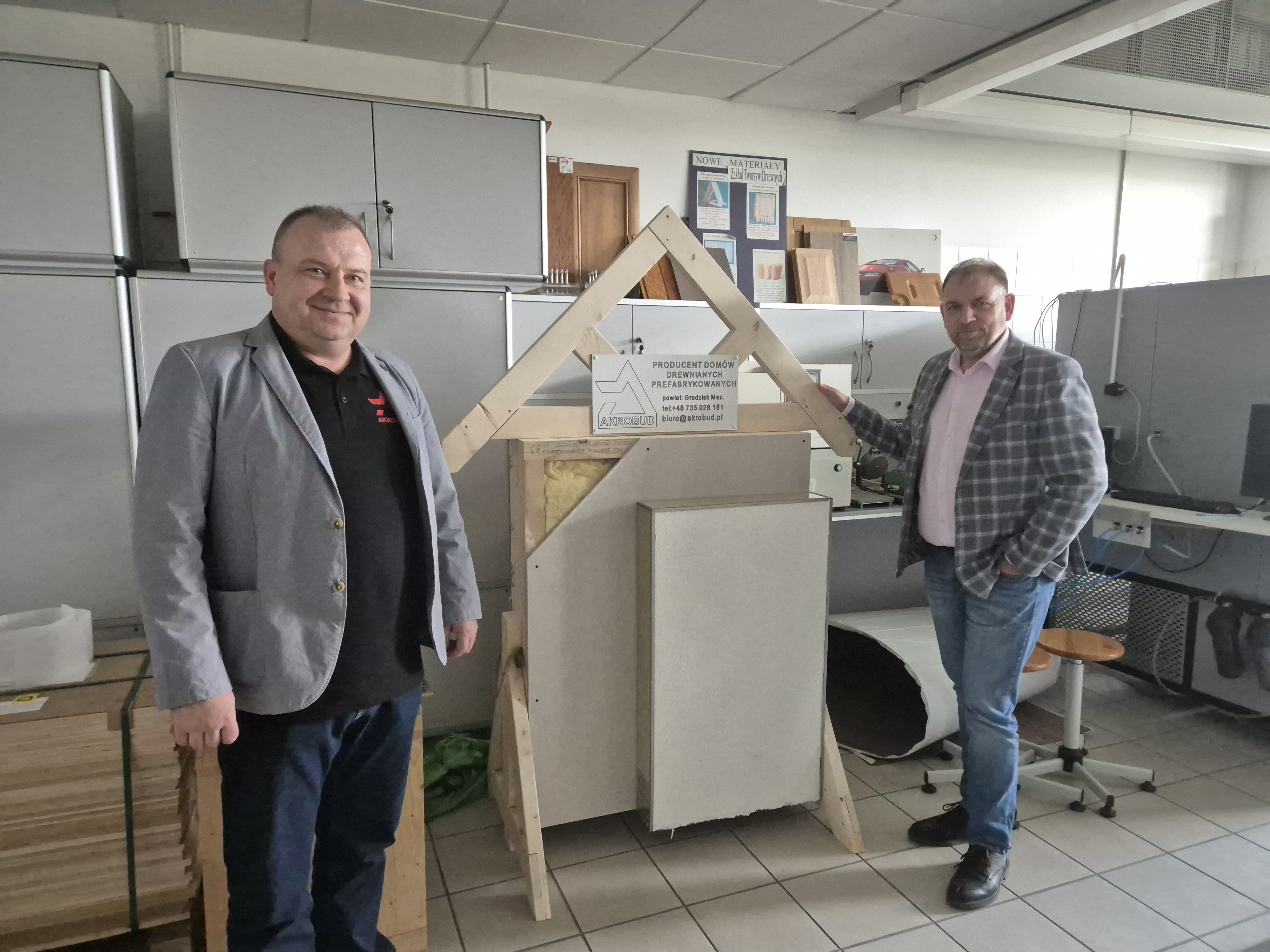 Dwóch mężczyzn w średnim wieku stojący obok ścianki ekspozycyjnej prezentującej przekrój ściany prefabrykowanej