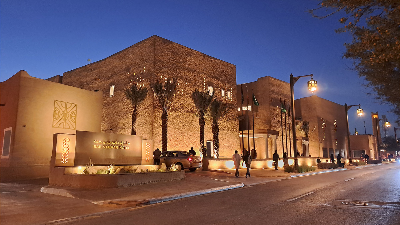 Close-up of a hand pouring a drink from a shaker into a martini glass with an orange garnish, set against a dark background.