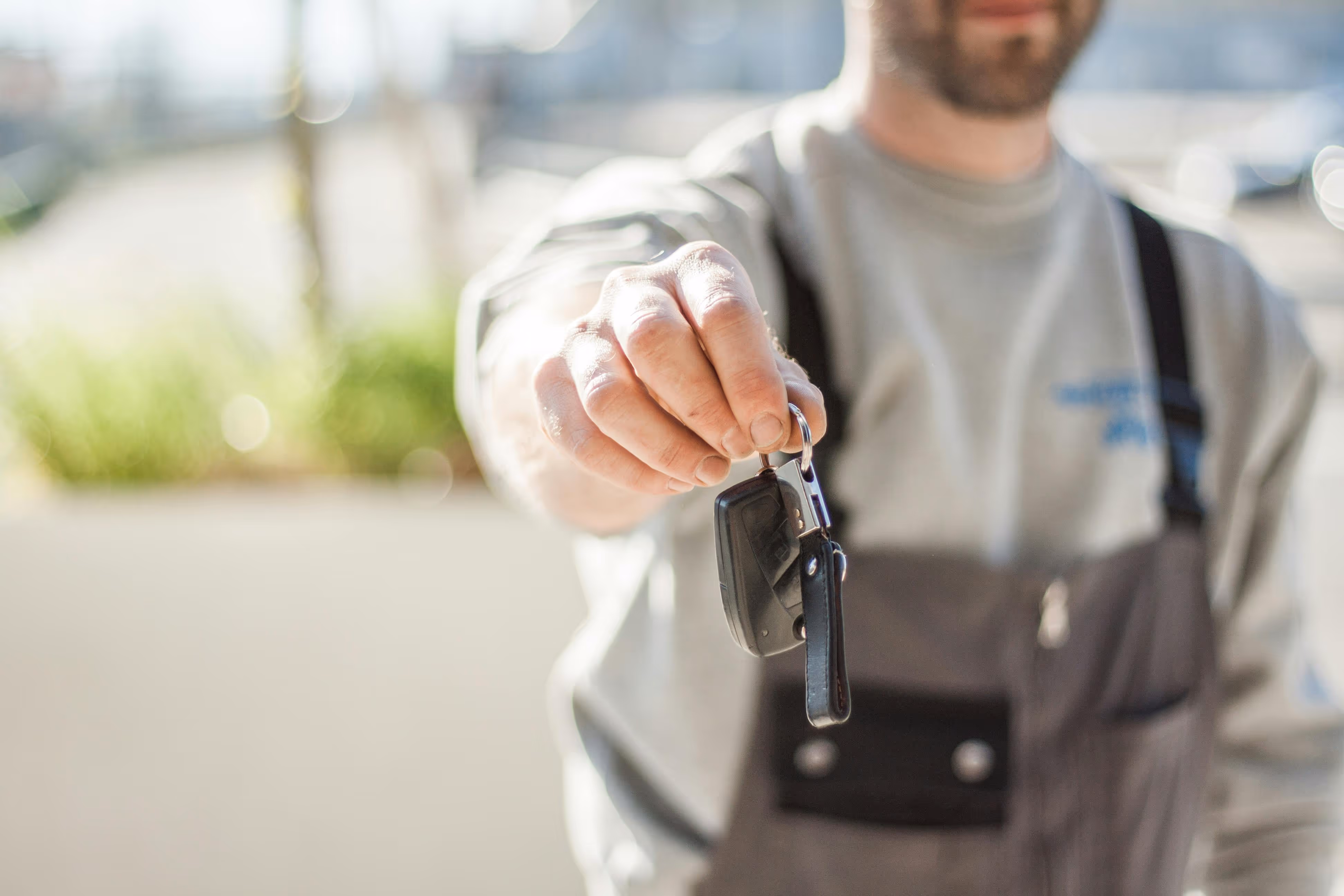 Man in overalls holding out a set of car keys towards the camera.