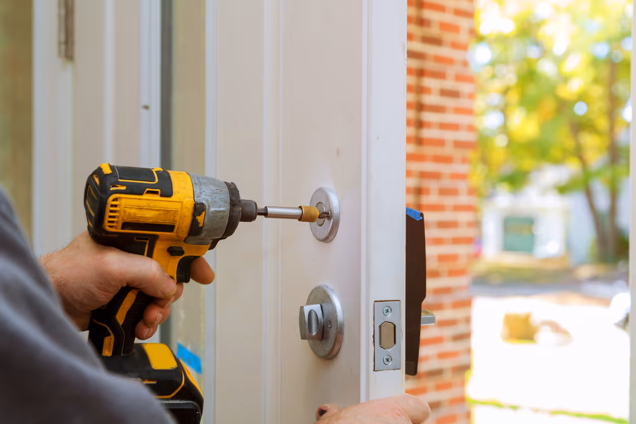 Person using a yellow cordless drill to install or repair a door lock on a white door.