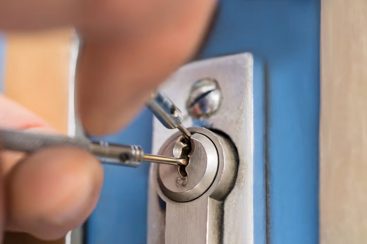 Close-up of a hand using lock picking tools on a silver door lock with a blue door background.