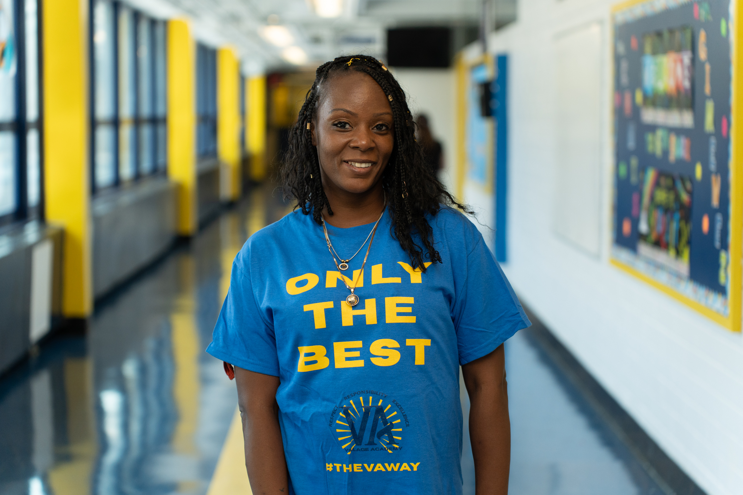 Ms. Georges smiling in school hallway wearing Only The Best shirt