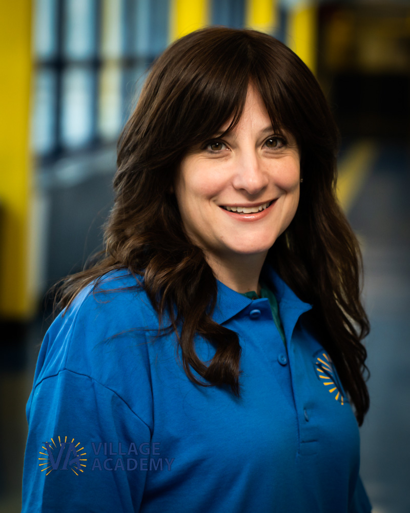 Ms A Sokel Village Academy staff member smiling in blue polo