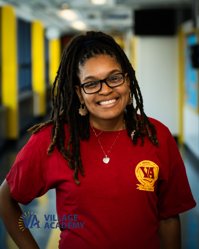 Ms. Thompson smiling in Village Academy shirt in school hallway