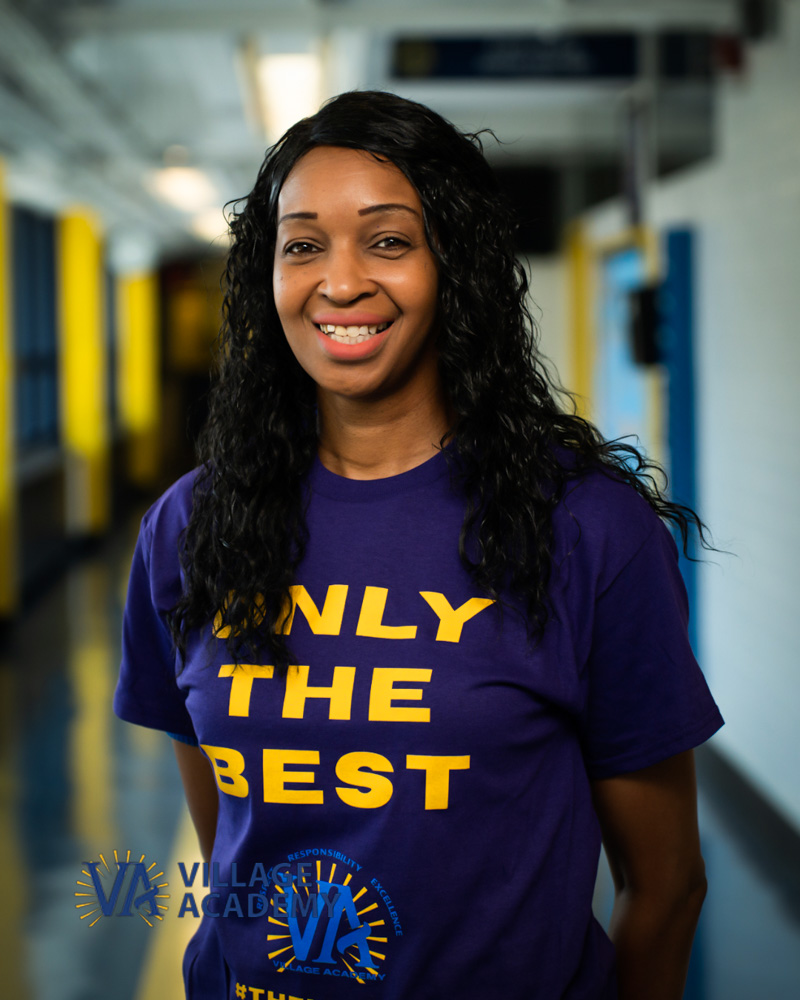 Ms. Thornton smiling in a Village Academy shirt in school hallway