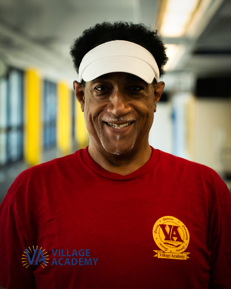 Mr. Burnett smiling in Village Academy shirt and white visor