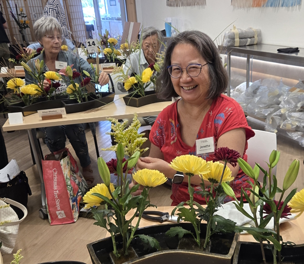 Jonette smiles while creating an Ohara School Rimpa-cho ikebana arrangement with chrysanthemums and lilies during Jose Salcedo’s August 2026 seminar in Columbus.