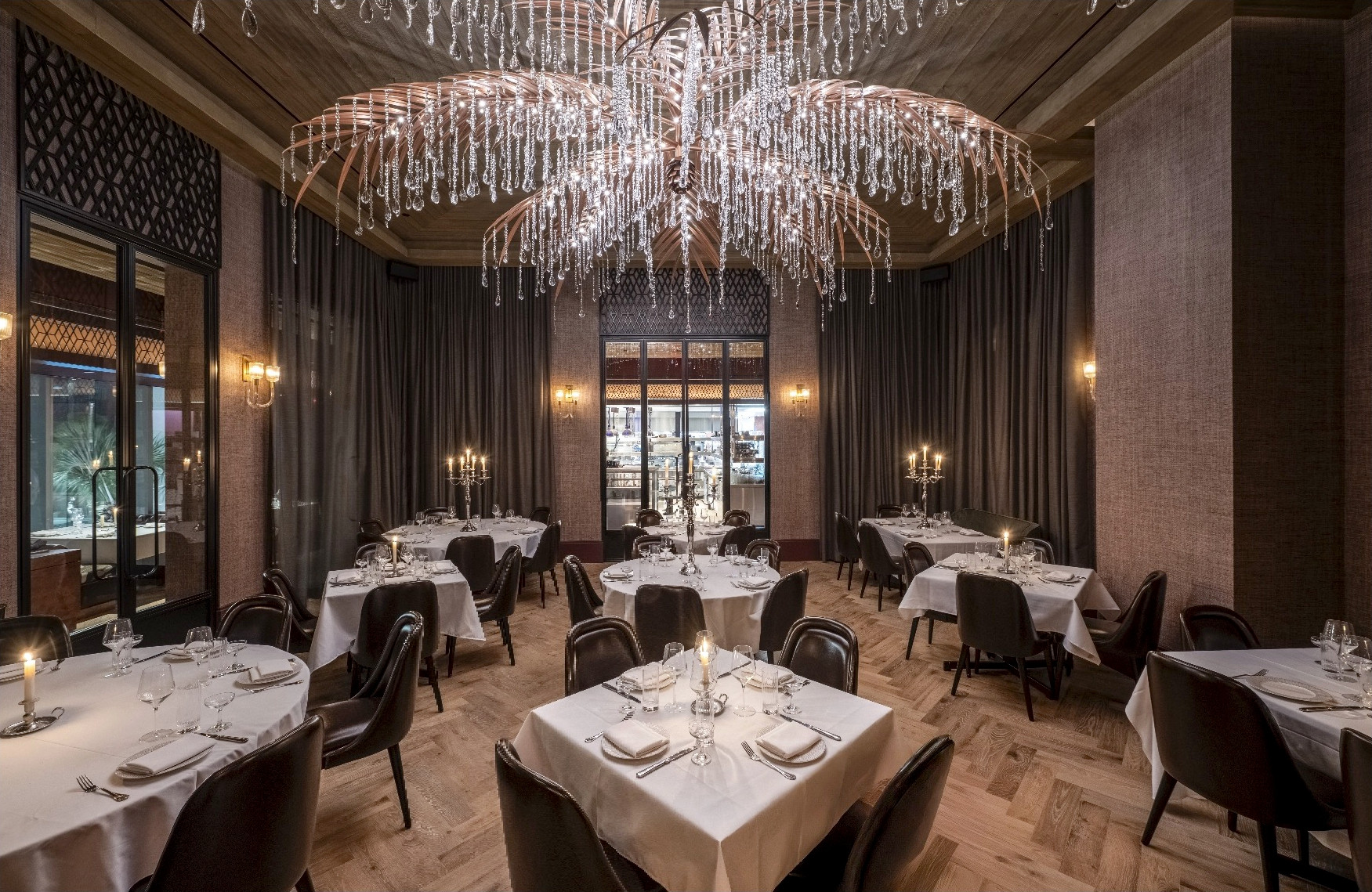 Elegant private dining room with white tablecloth tables, dark drapery, and a dramatic crystal chandelier.