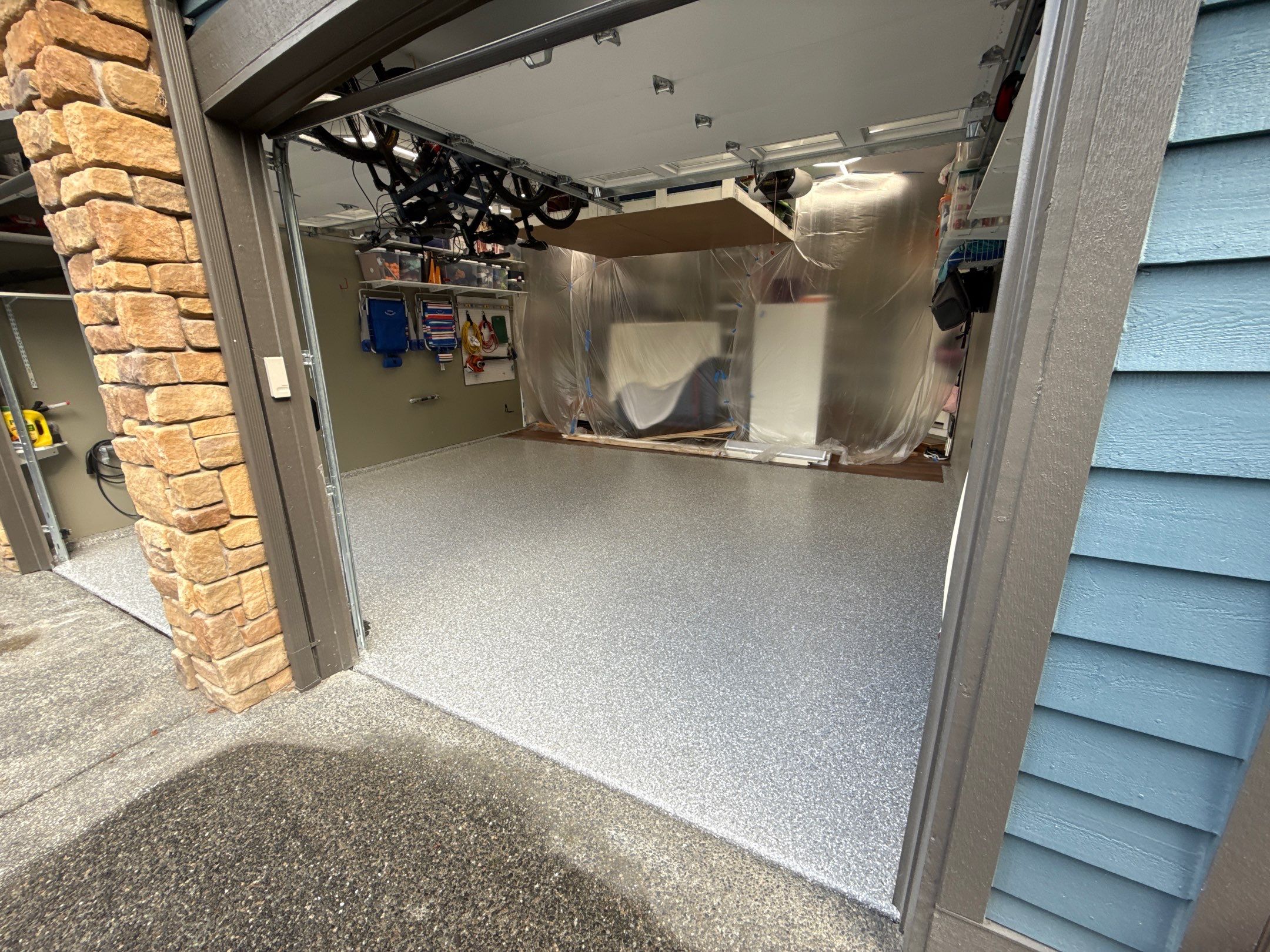 Single garage bay beside a stone column with a new light flake floor in Bothell