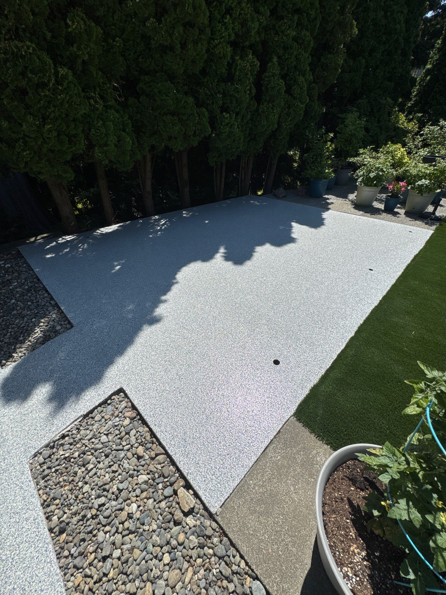 Tidal Wave flake polyurea patio beside the lawn and river rock border in Bothell