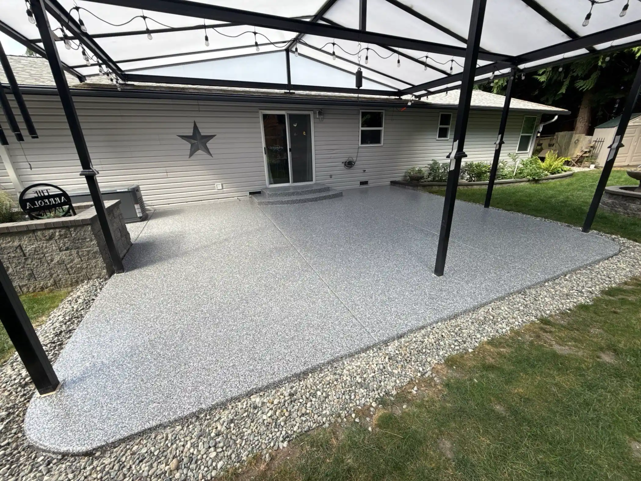 Smoke flake polyurea patio under a black pergola with a clear roof in Stanwood