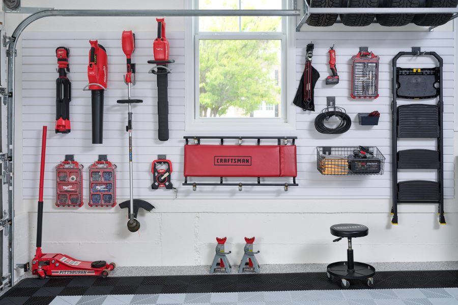 Garage wall system with neatly arranged power tools, automotive equipment, and accessories hung on slatwall panels beneath a window.