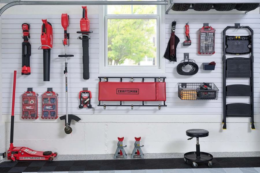 White garage slatwall system organizing power tools, hand tools, cords, baskets, ladder, and automotive equipment.