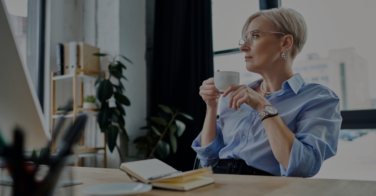Woman at her desk holding a cup of coffee, gazing out the office window
