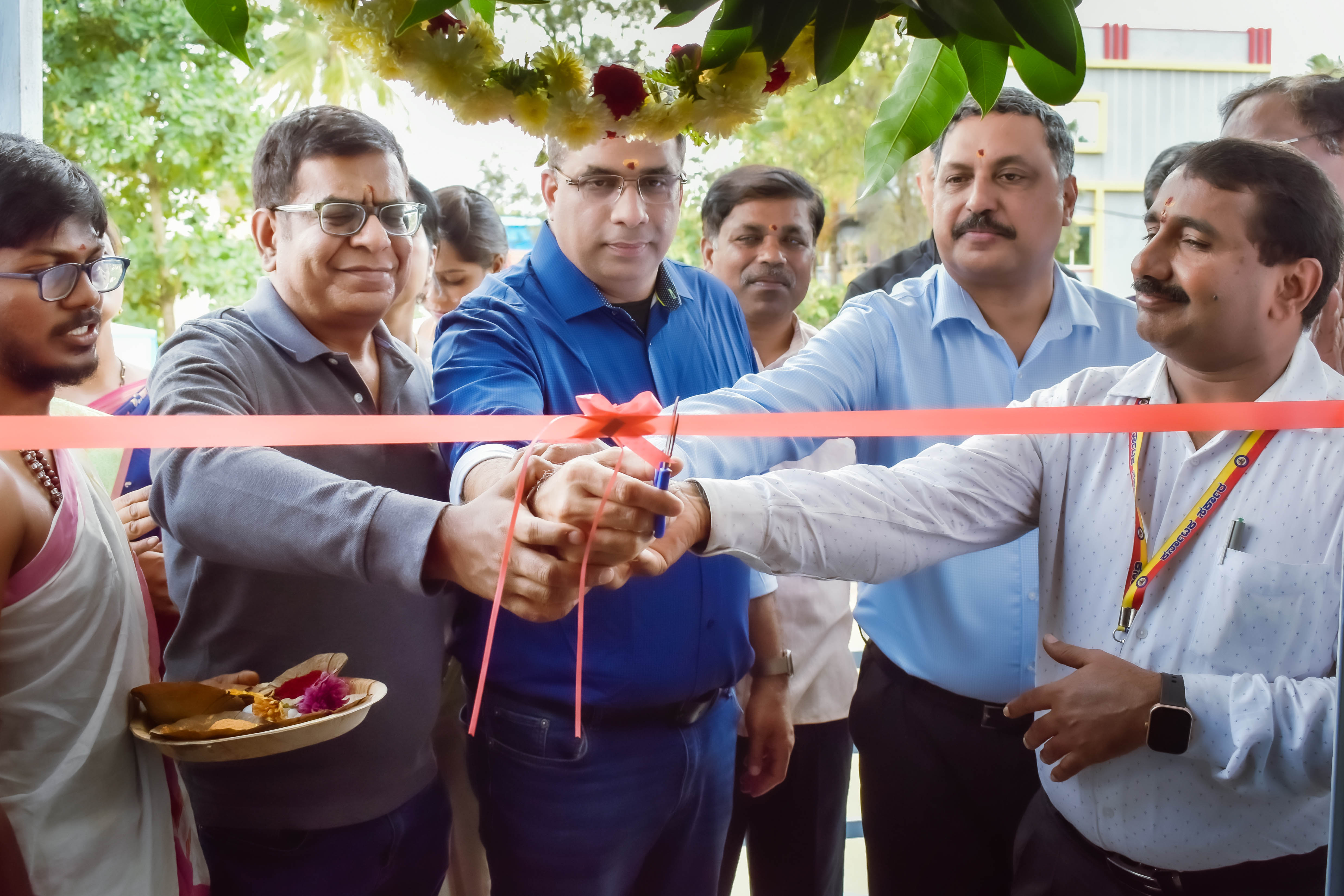 Group of people gather to cut a red ribbon during an inauguration ceremony, with festive decorations in the background.