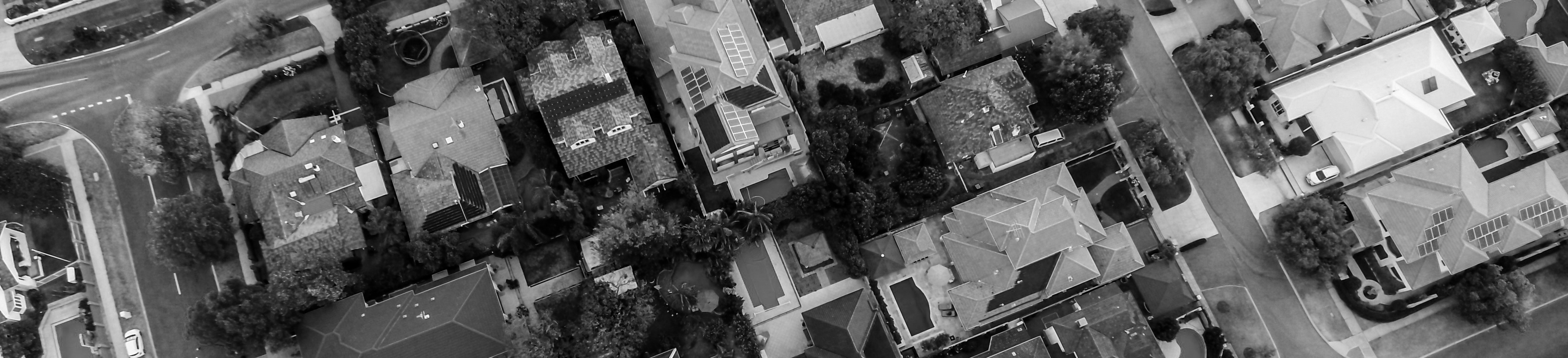 Aerial black and white view of a suburban neighborhood showing houses, trees, roads, and driveways.