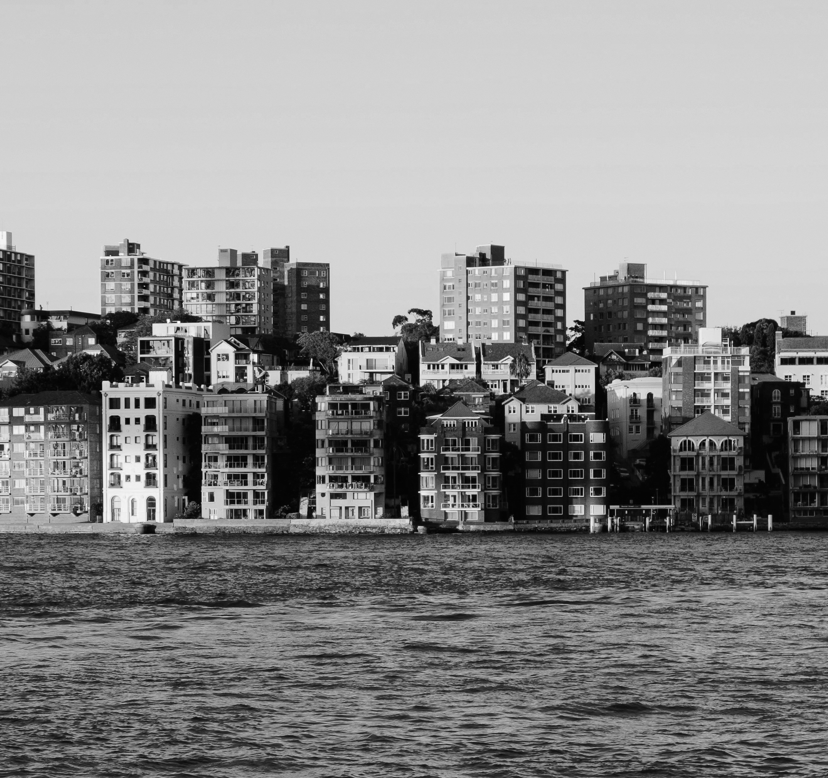 Black and white image of a waterfront cityscape with multiple mid-rise residential buildings.