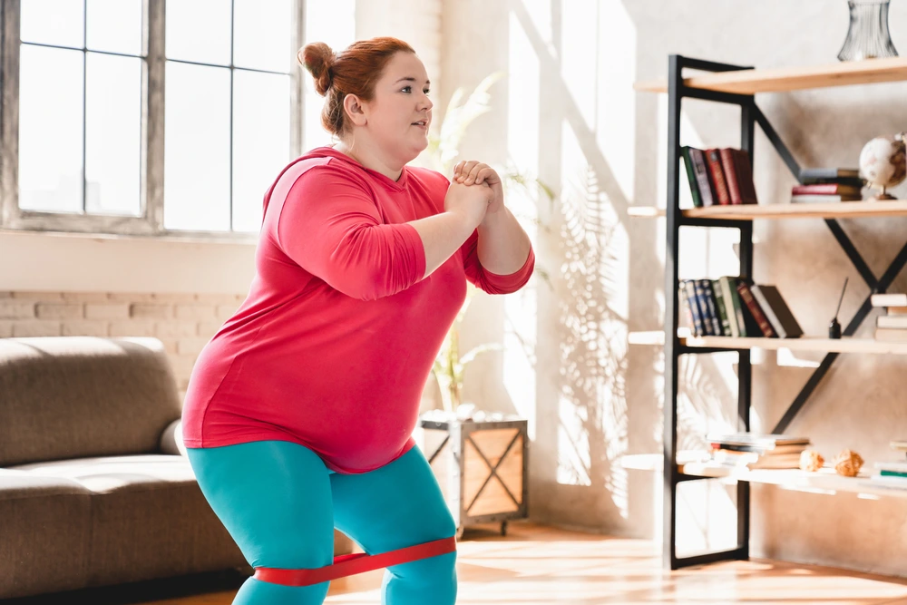 Frau mit Übergewicht trainiert zu Hause mit einem Fitnessband, um durch regelmäßige Bewegung langfristig abnehmen zu können.