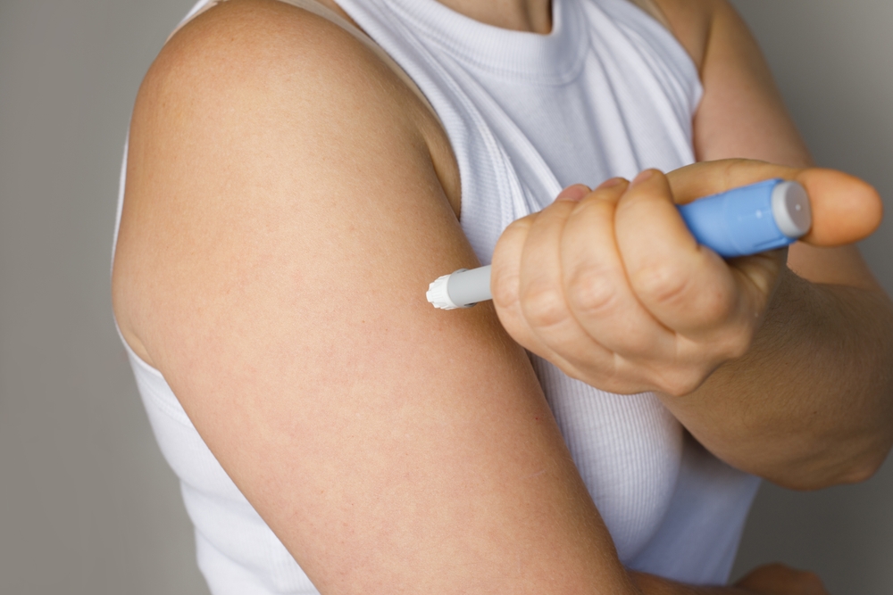 Person setzt einen Injektionspen am Oberarm an, um Insulin zum abnehmen zu verwenden.